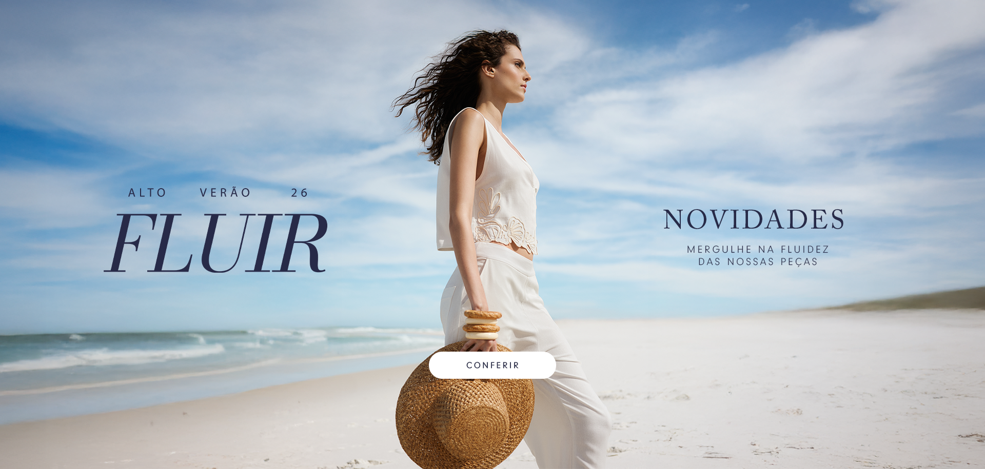 Mulher sentada em uma praia de areia clara, usando um vestido branco com alças finas e bordados florais. O texto sobreposto diz “FLUIR – Alto Verão 26” e “Novidades – Sinta o frescor da nossa nova coleção”.