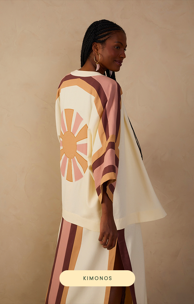 Banner em close com modelo negra de costas com foco em nosso Kimono Linho Recortes Bordados. A peça é fluida e fresca trazendo a essência da coleção Verão 26 Dress To – Refúgio, em fundo bege suave. CTA pílula verde-escuro no rodapé central com o texto “KIMONOS”.