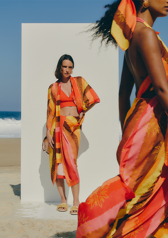 Modelo na praia com conjunto saia e kimono estampados e top laranja, coleção praia à vista