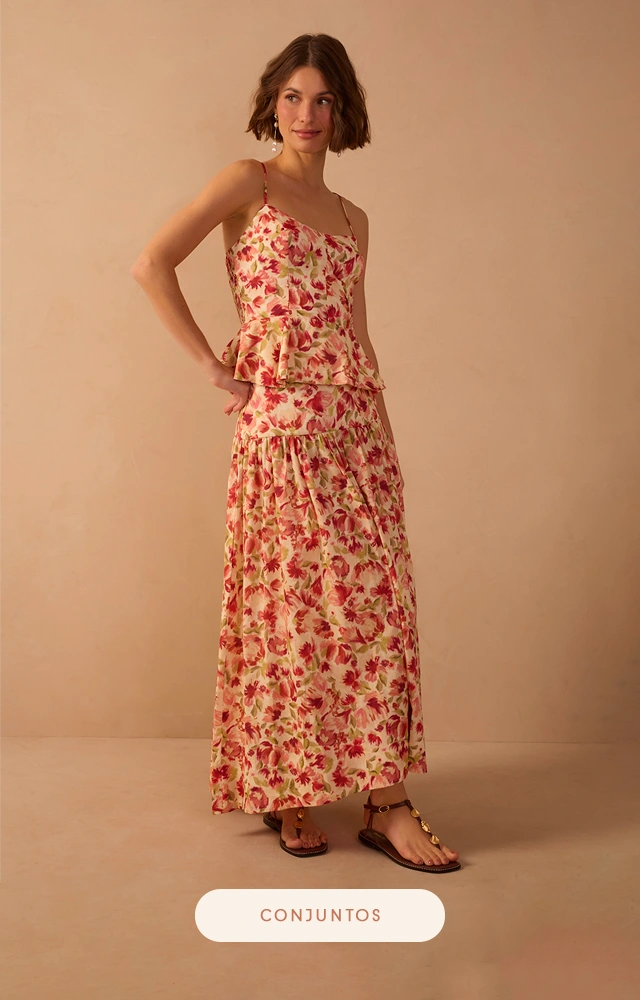 Modelo veste conjunto  feminino estampado floral com blusa de alças finas e saia longa fluida, em tons suaves de rosa e vermelho, ideal para looks elegantes e românticos.