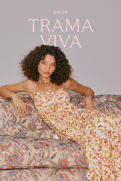 Banner da coleção Trama Viva com vestido longo floral de alças finas em tons suaves, combinado com acessórios dourados e sofá estampado com motivos florais.
