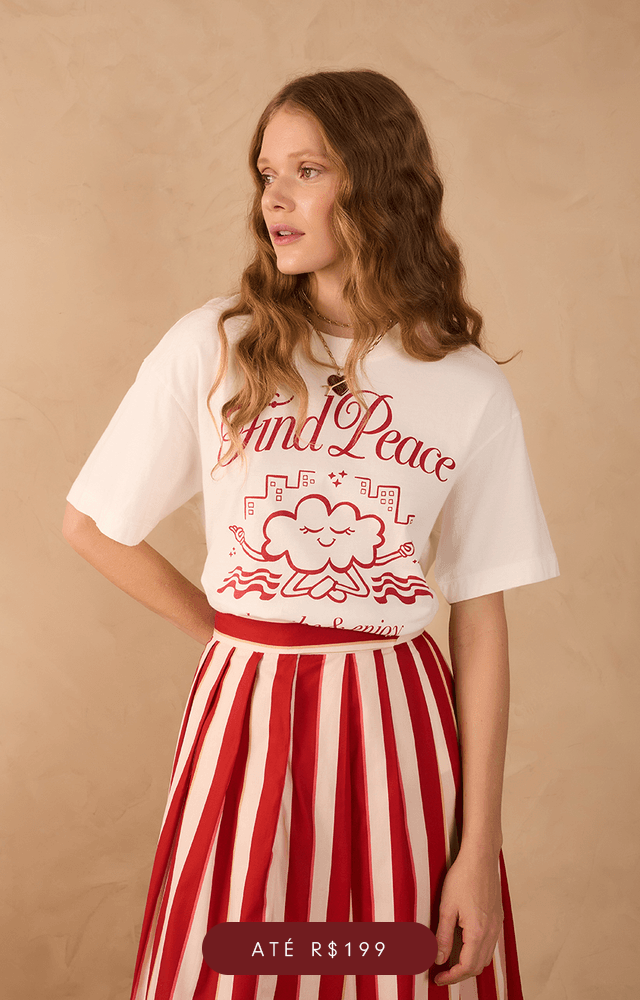 Modelo de pele clara e cabelos ruivos ondulados posa contra uma parede bege texturizada, vestindo um vestido longo tomara que caia com estampa listrada em tons de vinho e terracota, decorado com ilustrações douradas inspiradas em astros. Ela usa sandálias rasteiras trançadas e um colar com pingente em formato de coração. Abaixo da imagem, botão com a palavra 'Vestidos'.