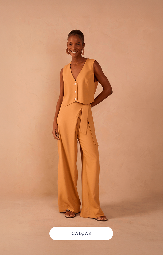 Modelo feminina em pé contra fundo bege, usando conjunto azul claro em tricô vazado. O look é composto por calça pantalona de caimento fluido e blusa longa sem mangas, aberta na frente. Nos pés, rasteira dourada.