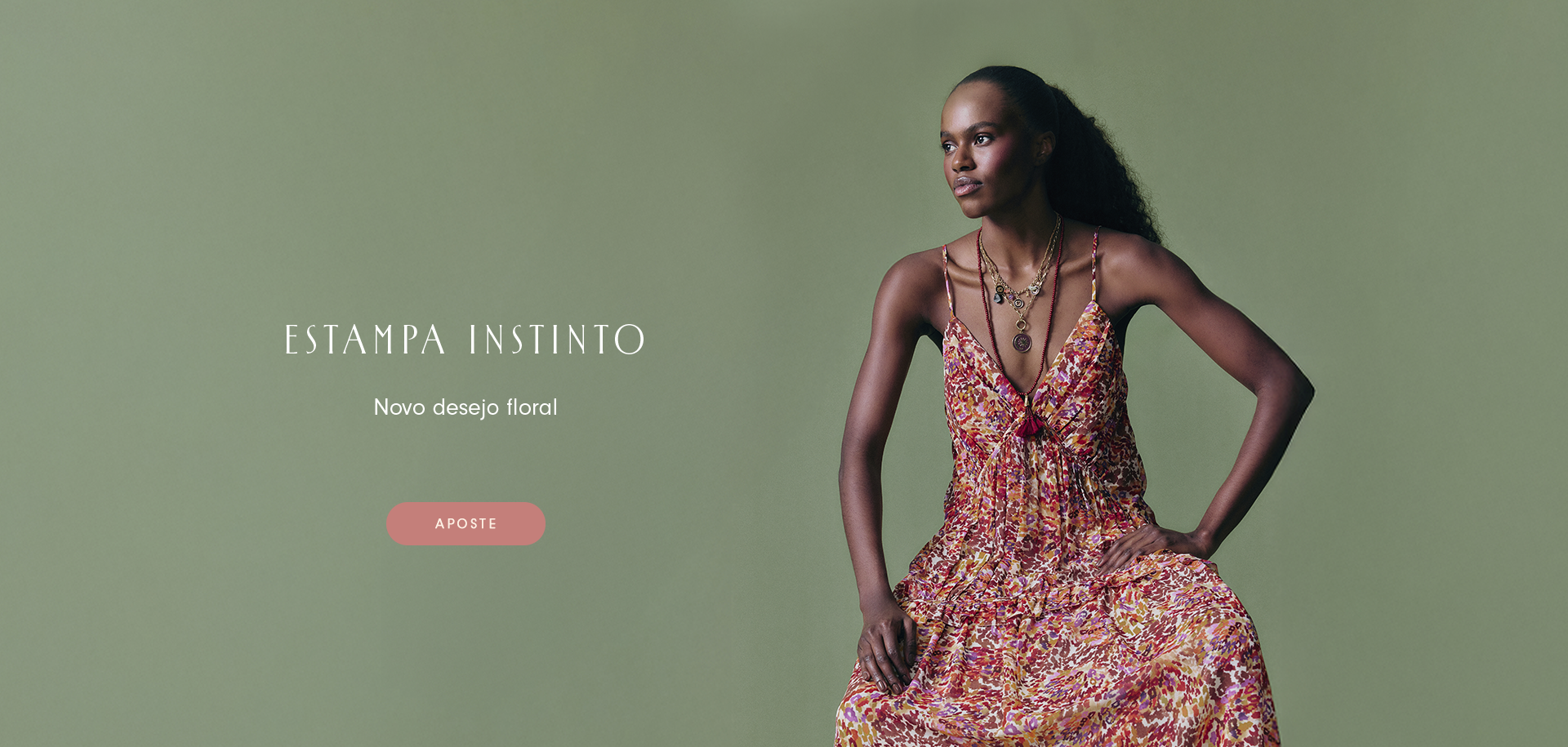 Banner com modelo negra com cabelo preso  usando vestido longo floral de alças finas em tons quentes, sobre fundo verde suave. Texto: “Estampa Instinto – Novo desejo floral” com botão “Aposte”. Visual elegante e minimalista destacando a nova estampa da coleção feminina.