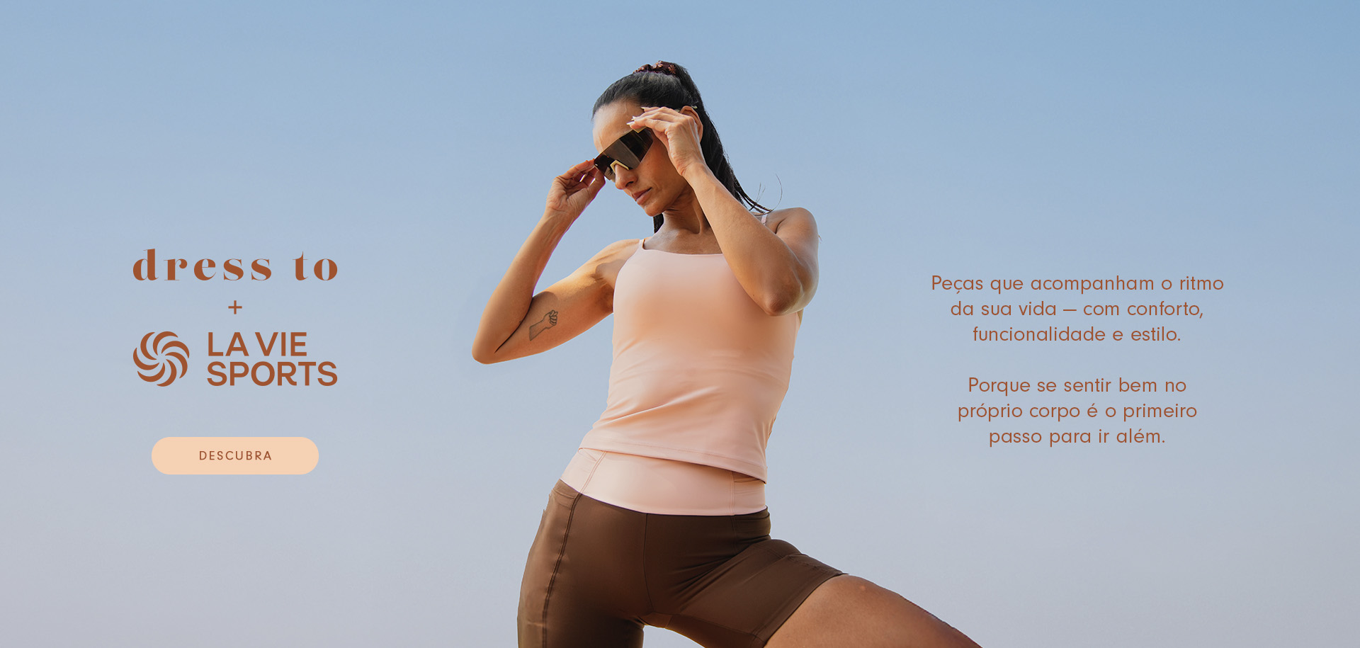 Modelo morena de cabelo preso veste roupa de treino, composta por regata de alça fina na cor rosa bebe e short de compressão na cor marrom  com bolso e cintura do short na cor rosa bebe, e para complementar o look ela esta usando óculos  de corrida. No texto do banner do lado esquerdo esta escrito " Dress to + La vie sports" abaixo do texto tem o botão na cor rosa escrito descubra. Ao lado direito tem o texto Peças que acompanham o ritmo da sua vida - com conforto, funcionalidade e estilo. Porque se sentir bem no próprio corpo é o primeiro passo para ir além.  