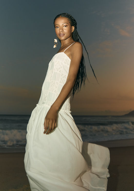 Modelo negra usando trança e vestido branco longo de alcinha com detalhes em renda da coleção de alto verão 25 da nova coleção calmaria da Dress To.