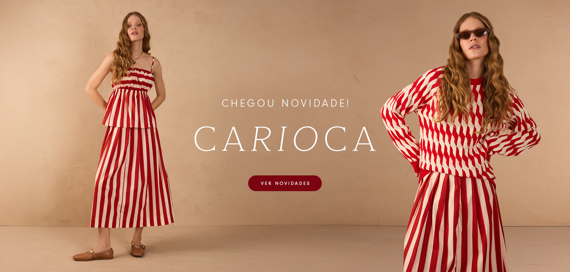 Duas mulheres posam em um ambiente neutro, usando peças da nova coleção Carioca. À esquerda, uma usa um conjunto de blusa de alças e saia midi com listras verticais vermelhas e brancas. À direita, outra modelo veste um suéter de tricô com padronagem ondulada vermelha e branca, combinado com a mesma saia listrada. Texto na imagem: 'Chegou novidade! Carioca. Ver novidades'.