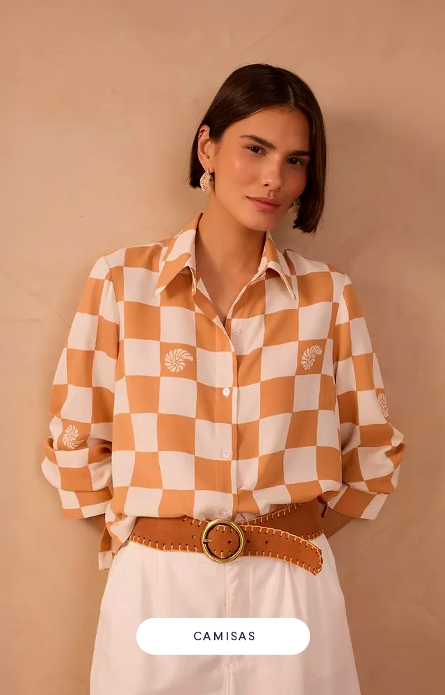 Modelo feminina contra fundo bege, vestindo conjunto branco em tecido vazado com recortes geométricos. A parte de cima é uma camisa de manga longa e a de baixo, shorts de cintura alta no mesmo tecido.