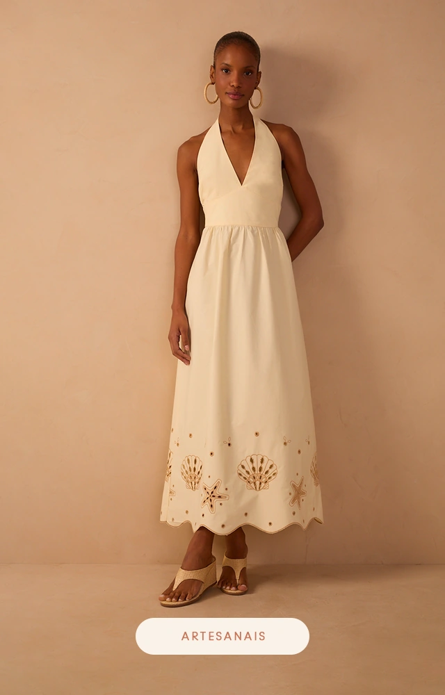 Vestido longo off-white com decote halter e recortes artesanais vazados na barra, confeccionado em tecido leve e elegante para ocasiões especiais.