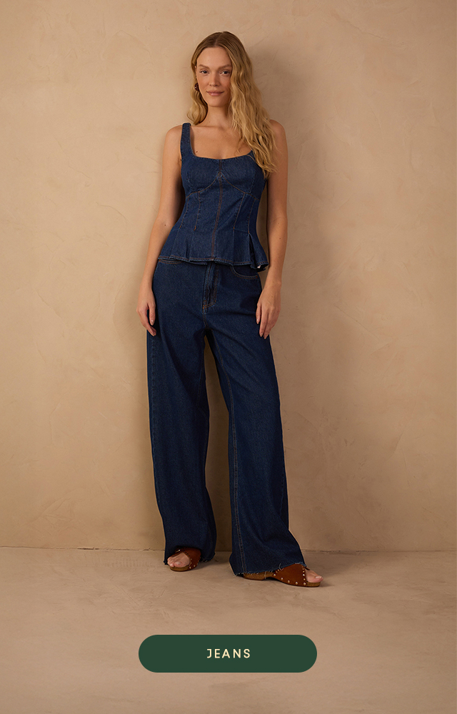 Banner da Dress To em tom bege suave. Modelo loira veste look casual composto por calça jeans off-white de cintura alta e jaqueta combinando, com blusa canelada marrom por baixo. Abaixo, botão verde com a palavra "JEANS".