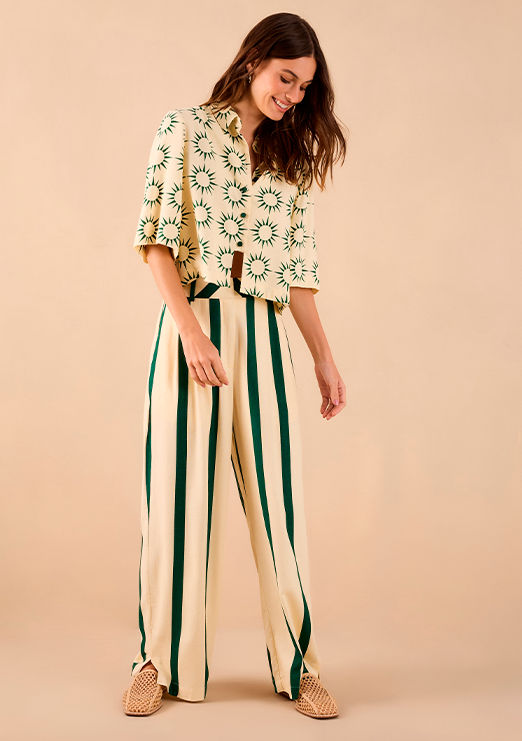 Modelo morena usando camisa com estampa de sol e calça listrada nas cores verde e offwhite.