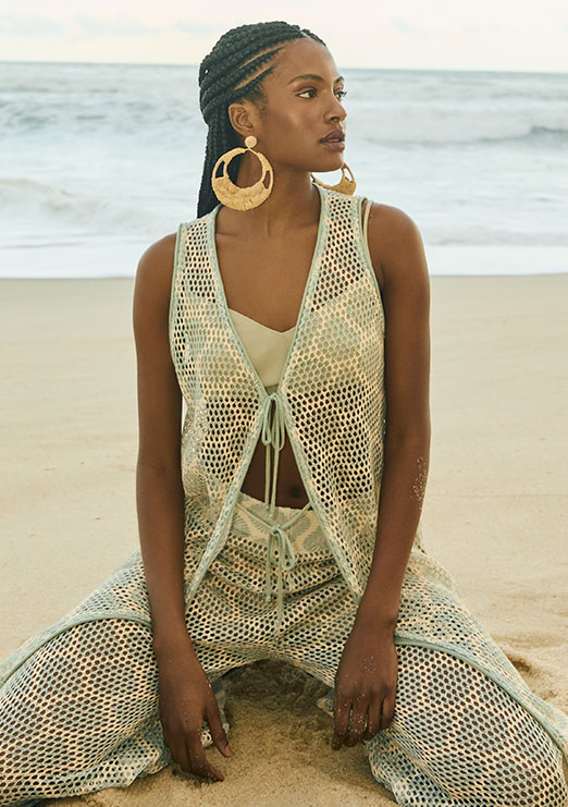 Modelo negra de trança usando conjunto de tricot posando em areia da praia. 