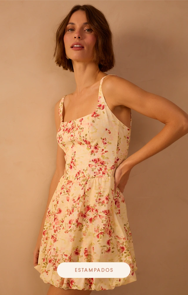 Modelo veste vestido curto estampado floral em tons suaves, com alças finas, decote reto e saia fluida, ideal para looks femininos e leves.