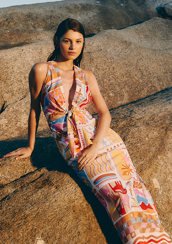 Modelo sentada na pedra, na praia, com vestido midi estampado da coleção Love, Dress.